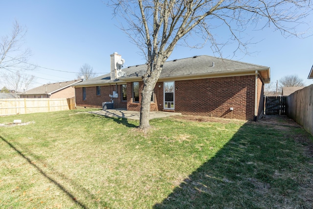 rear view of property with a chimney, brick siding, a yard, and a fenced backyard