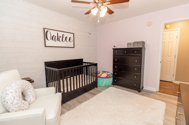 bedroom featuring a ceiling fan, light wood-type flooring, a crib, and baseboards