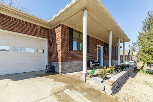 view of side of property with a garage, driveway, brick siding, and covered porch