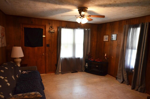 sitting room with ceiling fan, wooden walls, and a textured ceiling