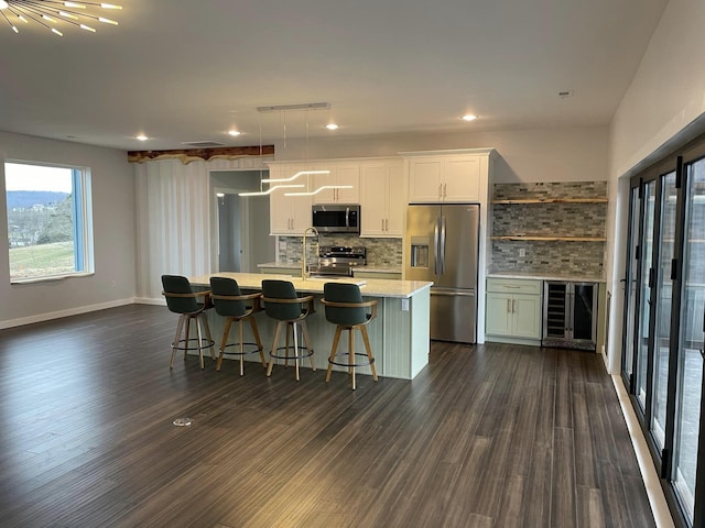 kitchen with appliances with stainless steel finishes, dark hardwood / wood-style floors, tasteful backsplash, an island with sink, and white cabinets