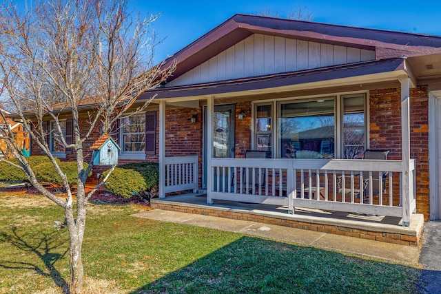 view of front of property featuring covered porch, brick siding, and a front lawn