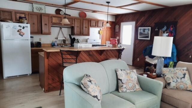 kitchen featuring wooden walls, open floor plan, light countertops, freestanding refrigerator, and brown cabinets