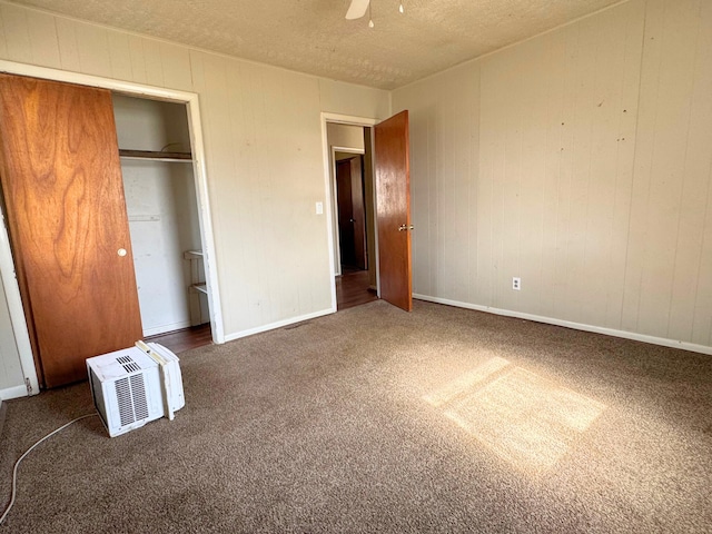 unfurnished bedroom with a closet, a textured ceiling, ceiling fan, dark colored carpet, and a wall unit AC