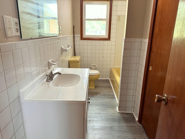 full bath featuring tile walls, toilet, vanity, wood finished floors, and a bathing tub