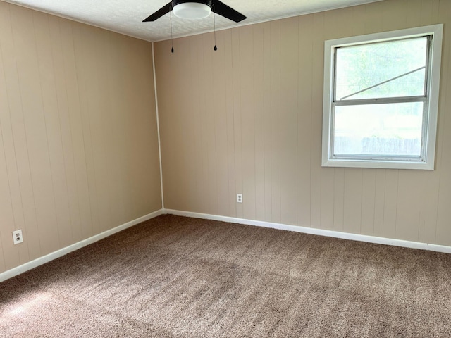 spare room with baseboards, wood walls, ceiling fan, and carpet