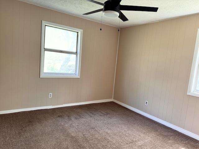 carpeted empty room with wooden walls, ceiling fan, and a textured ceiling