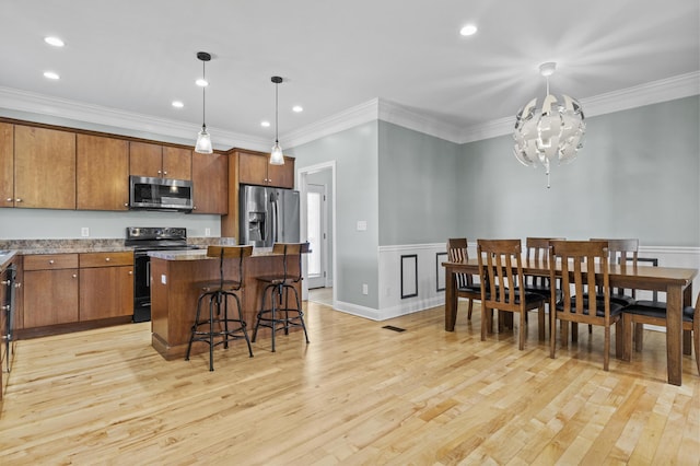 kitchen featuring appliances with stainless steel finishes, decorative light fixtures, a breakfast bar, a center island, and light wood-type flooring