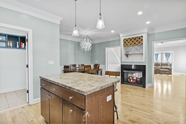 kitchen featuring a multi sided fireplace, a center island, pendant lighting, light hardwood / wood-style floors, and ornamental molding