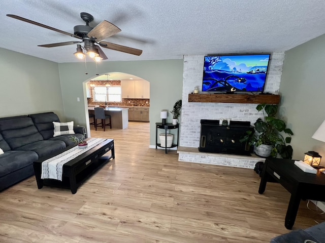 living room with a ceiling fan, arched walkways, light wood finished floors, and a textured ceiling