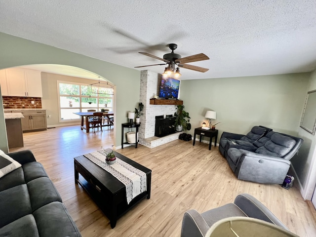 living area featuring a textured ceiling, a ceiling fan, arched walkways, and light wood-style floors