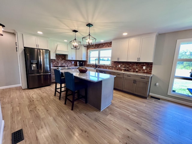 kitchen featuring visible vents, refrigerator with ice dispenser, light wood-type flooring, and premium range hood