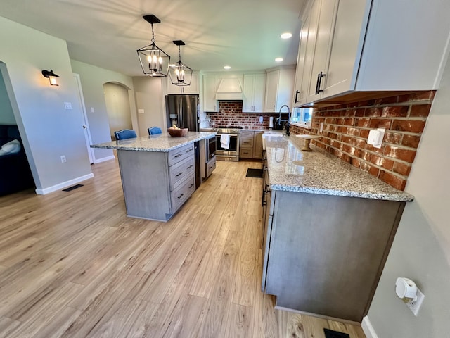 kitchen featuring light stone counters, tasteful backsplash, light wood-type flooring, stainless steel appliances, and arched walkways