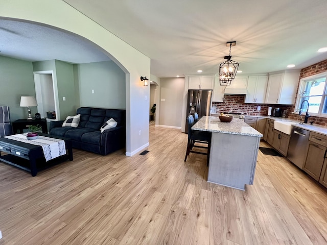 kitchen featuring a sink, a kitchen island, appliances with stainless steel finishes, light wood-type flooring, and arched walkways