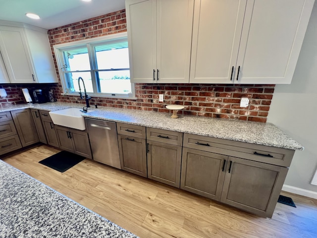 kitchen featuring backsplash, a sink, light stone counters, dishwasher, and light wood-style flooring