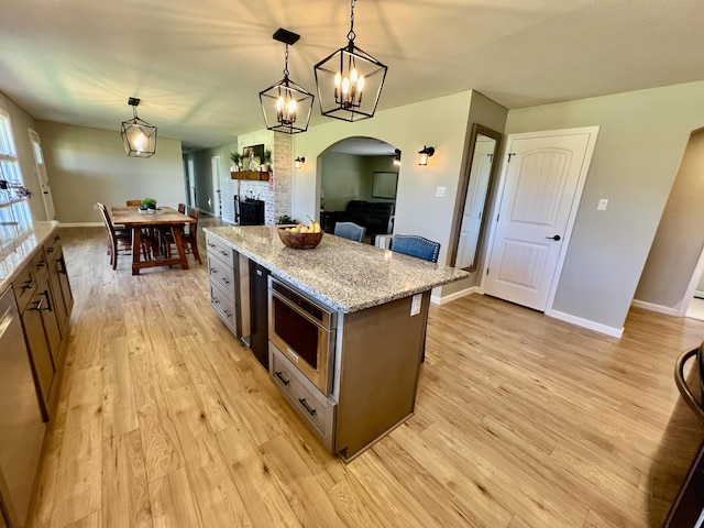 kitchen with a kitchen island, pendant lighting, light wood-type flooring, stainless steel appliances, and arched walkways