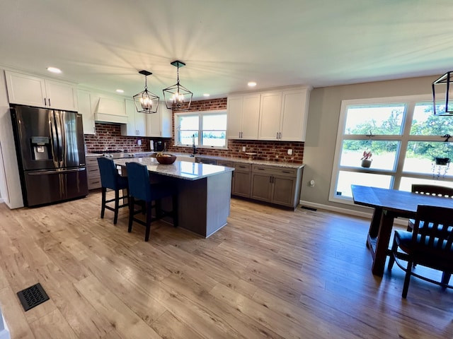 kitchen featuring white cabinetry, stainless steel fridge, light wood-type flooring, custom range hood, and a center island