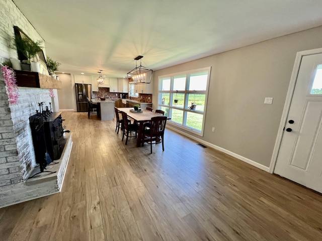 dining room with a notable chandelier, a fireplace, light wood-type flooring, baseboards, and visible vents