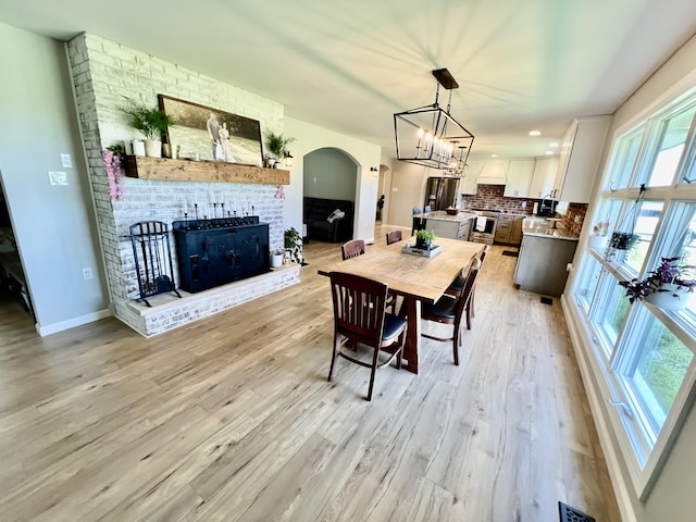 dining space featuring a brick fireplace, light wood-type flooring, baseboards, arched walkways, and an inviting chandelier