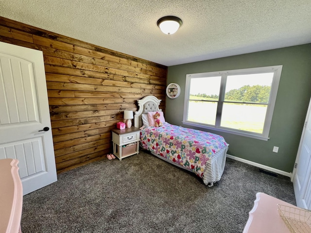 bedroom featuring a water view, wood walls, dark colored carpet, and a textured ceiling