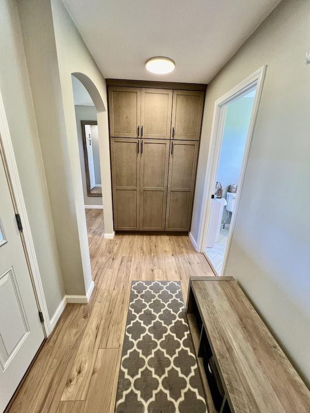 interior space featuring baseboards, light wood-type flooring, and arched walkways