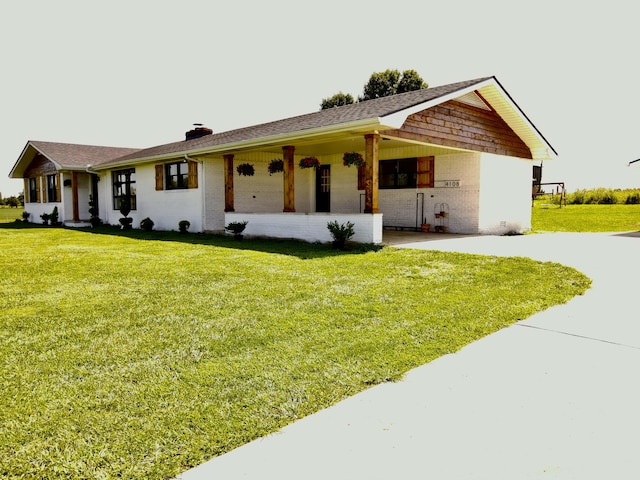 single story home featuring a chimney, concrete driveway, a front yard, brick siding, and a carport