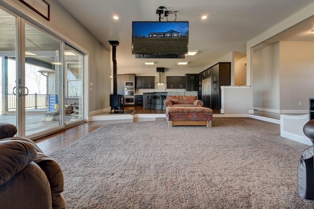 living area featuring a wood stove, recessed lighting, wood finished floors, and baseboards