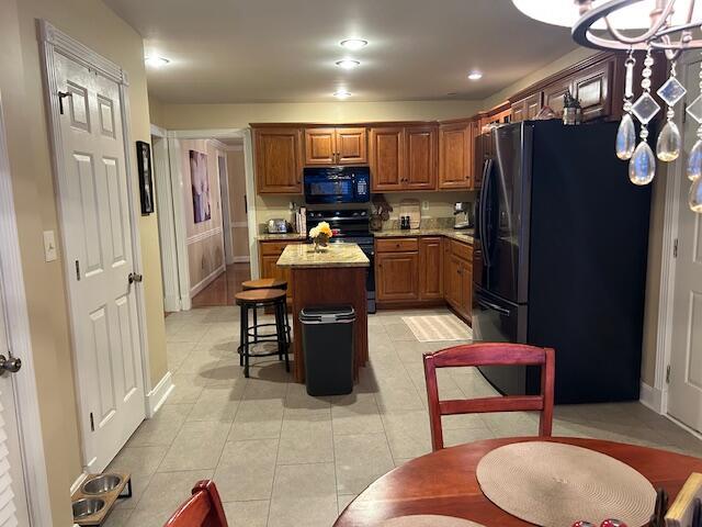 kitchen featuring light tile patterned flooring, a center island, a kitchen bar, and black appliances