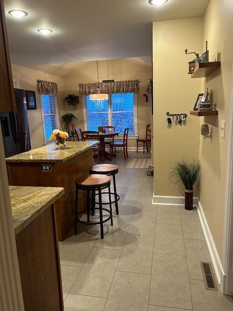 kitchen featuring black refrigerator, a center island, light stone counters, light tile patterned floors, and a breakfast bar area