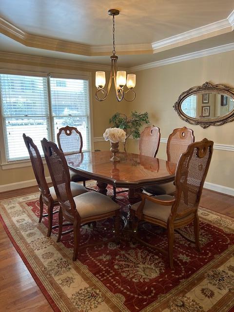 dining area with crown molding, hardwood / wood-style flooring, a tray ceiling, and a notable chandelier