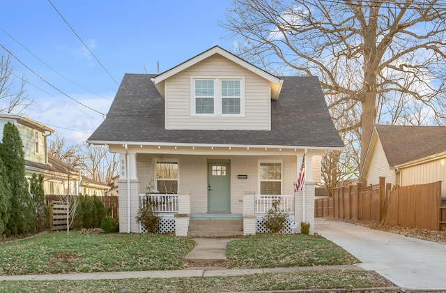 bungalow with covered porch, brick siding, fence, and roof with shingles