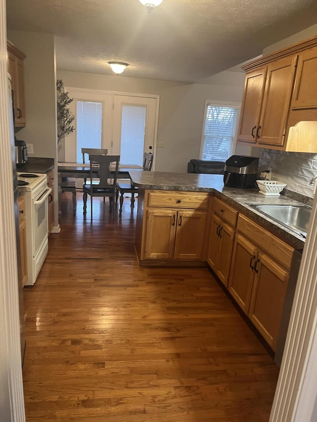 kitchen with dark countertops, dark wood finished floors, a peninsula, and electric stove