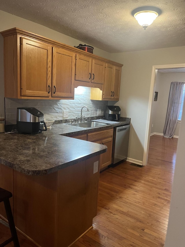 kitchen featuring dark wood-style floors, a peninsula, dishwasher, dark countertops, and backsplash