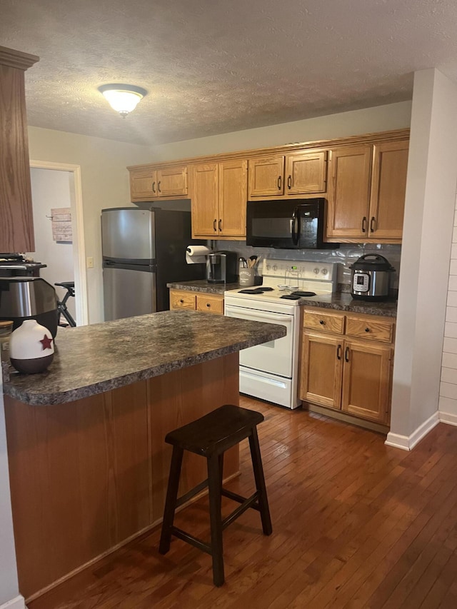 kitchen featuring dark countertops, black microwave, white range with electric cooktop, dark wood finished floors, and freestanding refrigerator