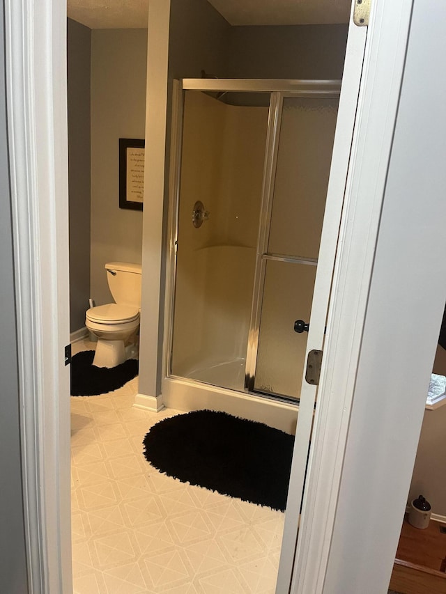 bathroom with tile patterned floors, a shower stall, toilet, and baseboards