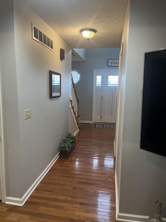 hall with visible vents, baseboards, stairway, hardwood / wood-style flooring, and a textured ceiling