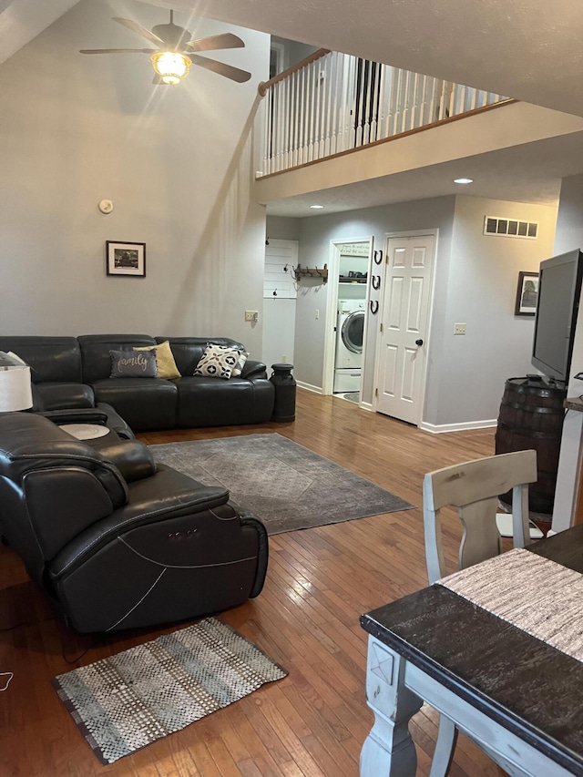 living room with visible vents, a ceiling fan, washer / clothes dryer, hardwood / wood-style floors, and a high ceiling