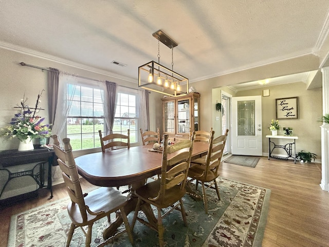 dining space with wood-type flooring, ornamental molding, and a textured ceiling