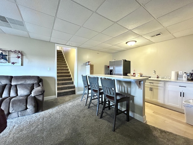 kitchen featuring white cabinetry, a paneled ceiling, stainless steel fridge, and a kitchen breakfast bar