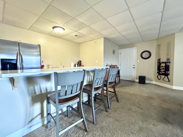 kitchen with a kitchen bar, a paneled ceiling, stainless steel fridge, kitchen peninsula, and carpet flooring