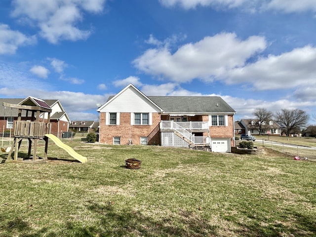 back of property with a garage, a lawn, a playground, and a fire pit