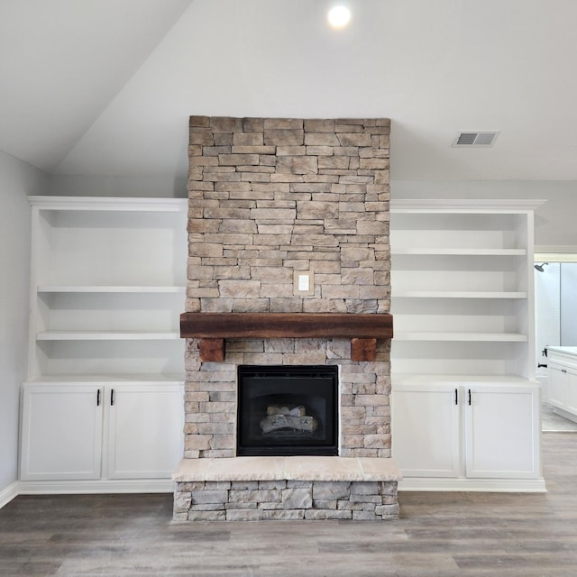 room details featuring built in features, visible vents, a stone fireplace, and wood finished floors