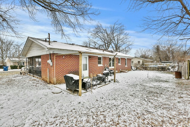 snow covered rear of property featuring brick siding