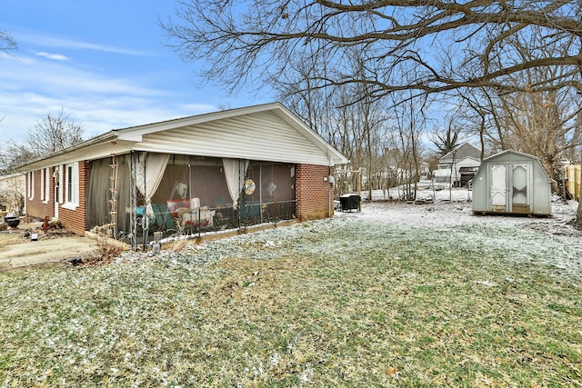 view of snow covered exterior featuring a sunroom, a shed, an outdoor structure, and brick siding