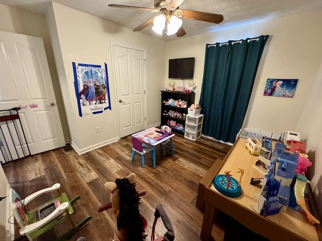 game room with dark wood-style flooring, ceiling fan, and baseboards