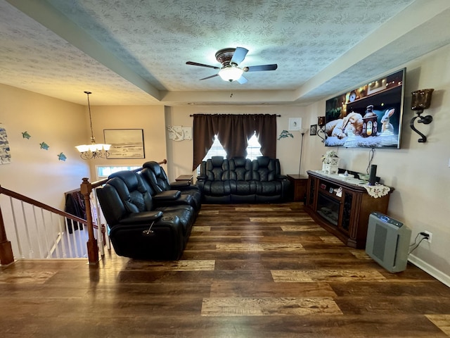 living room with a raised ceiling, dark wood-type flooring, a textured ceiling, baseboards, and ceiling fan with notable chandelier