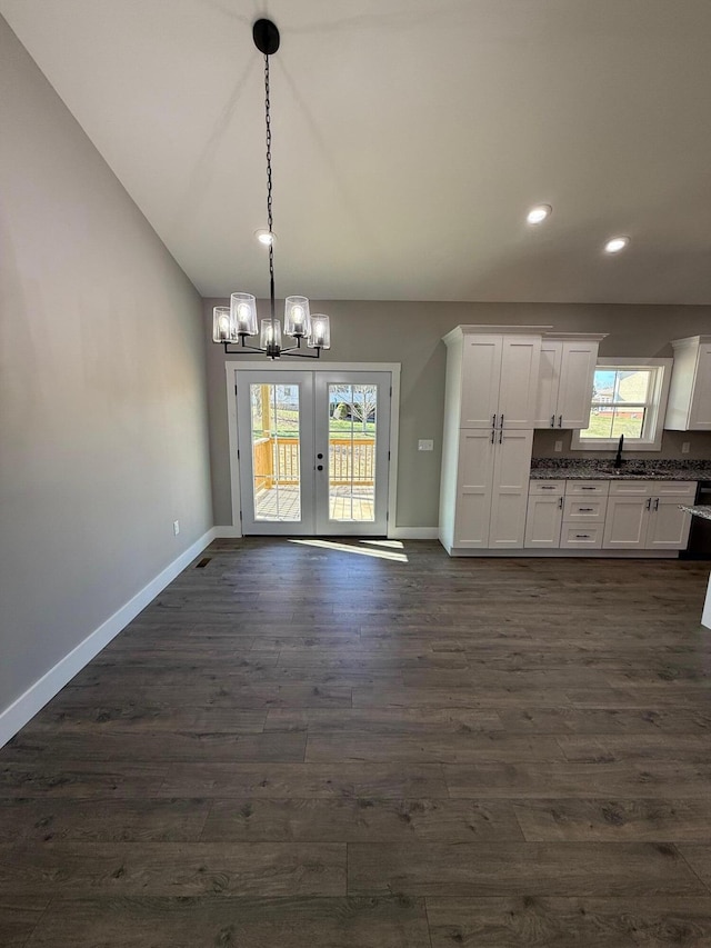 unfurnished dining area with sink, dark hardwood / wood-style floors, a notable chandelier, vaulted ceiling, and french doors