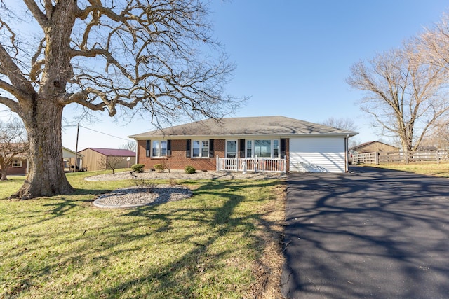 ranch-style home with aphalt driveway, covered porch, brick siding, fence, and a front lawn