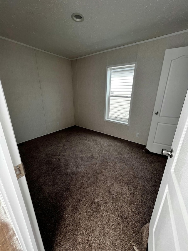 unfurnished bedroom featuring dark carpet, a textured ceiling, and ornamental molding