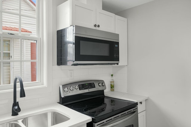 kitchen featuring a wealth of natural light, a sink, stainless steel appliances, white cabinetry, and backsplash